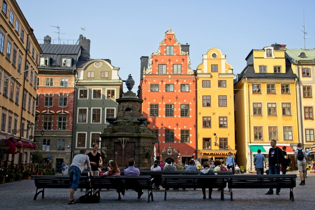 people sitting on bench near brown concrete building during daytime gamla stan gekleurde huisjes stockholm met kinderen oude binnenstad