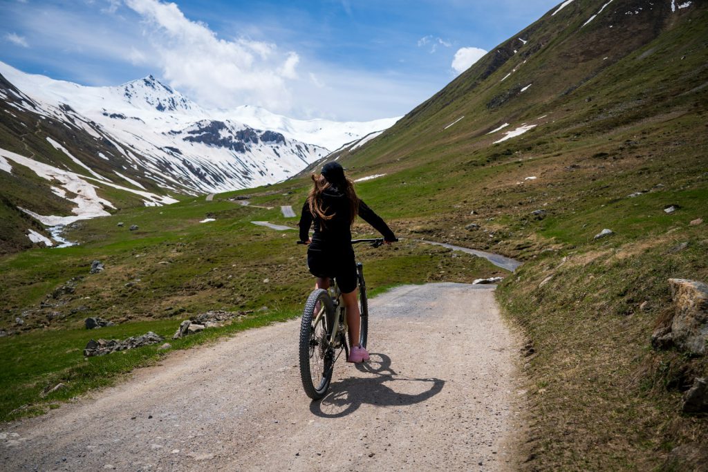 a woman riding a bike down a dirt road vrouw op de fiets op een grindpad in de bergen met sneeuw alpen